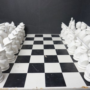 May include: A white chess set with all the pieces set up on a black and white checkered board. The pieces are all white and are made of a smooth, porcelain-like material.