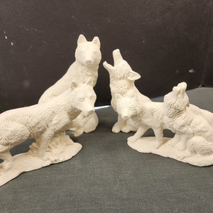 May include: Four white ceramic wolf figurines, each with a different pose. The wolves are arranged in a circle, with their heads tilted up as if they are howling.