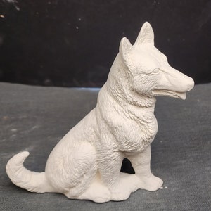May include: White ceramic figurine of a dog sitting with its head turned to the side. The dog has a detailed fur texture and is in a realistic pose.