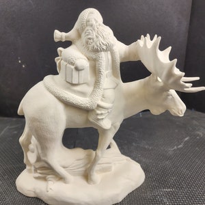 May include: A ceramic figurine of Santa Claus riding a moose. Santa is wearing a hat and coat with a fluffy trim, and he has a long beard. The moose has large antlers and is standing on a snowy base. The figurine is unpainted.