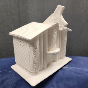 May include: White ceramic figurine of a building with a roller skate on the roof. The building has columns and a detailed facade.