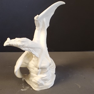 May include: White ceramic sculpture of a dragon with wings spread out. The dragon is perched on a rock base.