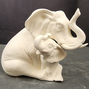 May include: A white ceramic sculpture of a mother elephant and her baby. The mother elephant is sitting with her trunk curled around her baby. The baby elephant is sitting upright with its trunk raised.