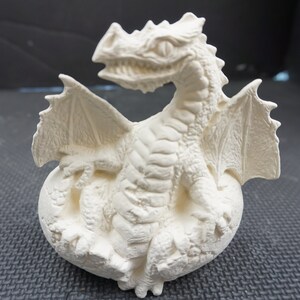 May include: A detailed, off-white dragon figurine with outstretched wings and a detailed, textured surface. The dragon is perched on a rounded base, with its mouth open, and its wings spread wide. The figurine is a fantasy-themed decorative item.