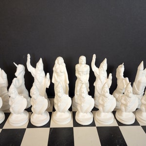 May include: A set of 16 white ceramic chess pieces, including a unicorn, a castle, and a variety of fantasy figures. The pieces are arranged on a black and white checkered chessboard.