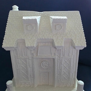 Puede incluir: Una figura de casa de cer&aacute;mica blanca con un tejado texturizado, dos chimeneas y marcos de ventanas y puertas detallados. La casa tiene una apariencia r&uacute;stica, tipo caba&ntilde;a, con una peque&ntilde;a chimenea y detalles decorativos.