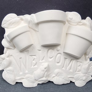 May include: White ceramic welcome sign with three flower pots and a frog. The sign says "WELCOME" in raised letters.