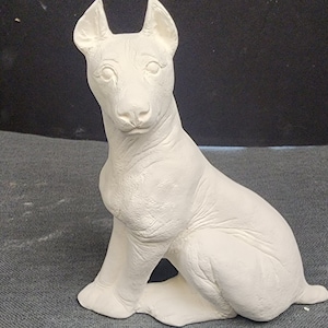 May include: White ceramic figurine of a dog sitting with its ears perked up. The dog has a detailed face with a defined nose and eyes.