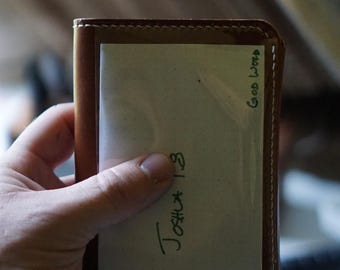 May include: A brown leather wallet with a white card insert. The card insert has the text "Joshua 1:3" and "Good Word" written in green ink.