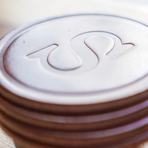 May include: Close-up of a brown, circular object with a white, stylized "S" design on top. The object has several stacked, ridged layers. The background is blurred, with a wooden surface in the foreground.