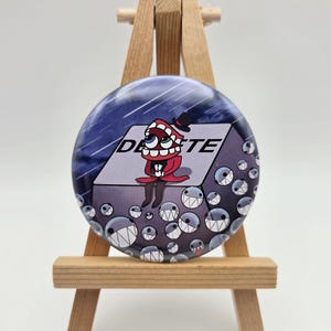 May include: A circular pinback button featuring a cartoon character with a large mouth and top hat sitting on a gray block labeled DELETE. The background is a dark blue sky with rain, and the foreground is filled with many small, round, toothy creatures.