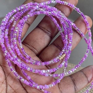 May include: A purple and silver beaded waist chain with multiple strands. The chain is made of small, round beads and is designed to be worn around the waist.