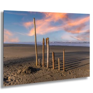 May include: A scenic beach landscape featuring several weathered wooden posts planted in the sand. The sky displays a vibrant mix of blue and orange hues, with the ocean visible in the background. The scene evokes a sense of tranquility.