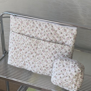 May include: Two quilted zippered pouches with a floral pattern. The larger pouch is white with pink flowers and the smaller pouch is white with green flowers.