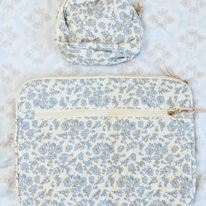 May include: Two quilted fabric items with a floral pattern. The larger item is rectangular with a zipper, and the smaller item is a rounded pouch with a zipper. Both items have a cream background with blue floral designs.