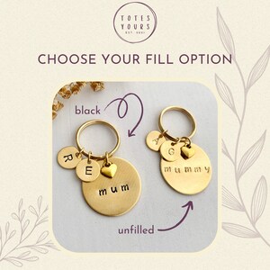 May include: Two gold-toned metal keychains featuring circular discs and heart charms. One keychain displays the word mum with black-filled lettering, while the other shows the word mummy with unfilled lettering. Additional small discs feature letters.