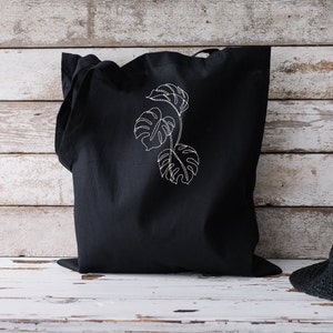 May include: A black tote bag with a white outline of a monstera leaf plant design.