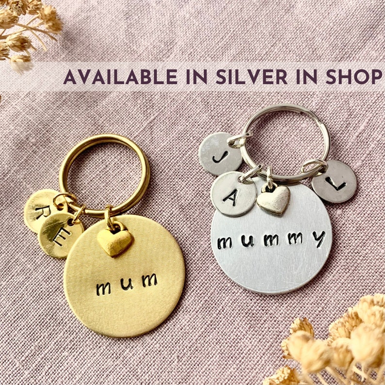 May include: Two circular metal keychains, one gold-toned and one silver-toned. The gold keychain features the word mum and two smaller discs with letters R and E. The silver keychain features the word mummy and three discs with letters J, A, and L.