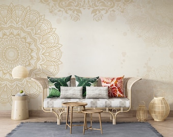 May include: A bohemian-style living room with a light beige wall featuring a large gold mandala design. A rattan sofa is adorned with patterned pillows. Two small wooden tables and a woven lamp are in front of the sofa. A woven lantern sits on the floor.