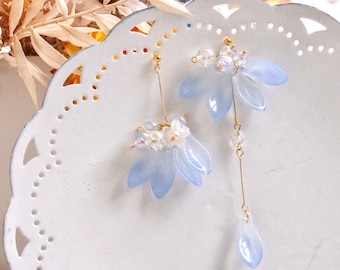 May include: A pair of delicate earrings featuring light blue flower-shaped charms with gold accents. The earrings are suspended from gold chains and adorned with small white beads.