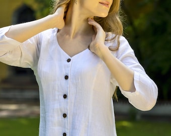 May include: A woman wearing a white linen dress with a button-down front. The dress has a v-neck and three-quarter sleeves.