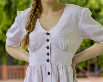 May include: A light pink linen dress with a v-neck and button-up front. The dress has a fitted bodice and a flowy skirt.