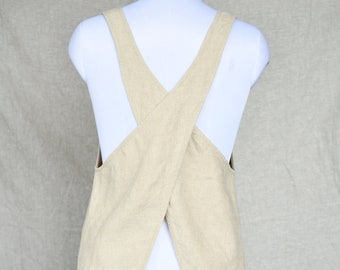 May include: A beige linen apron with a criss-cross back design. The apron is long and has a V-neck.