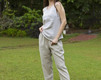 May include: A woman wearing a light gray sleeveless top and beige linen pants. She is standing in a grassy field and smiling at the camera.