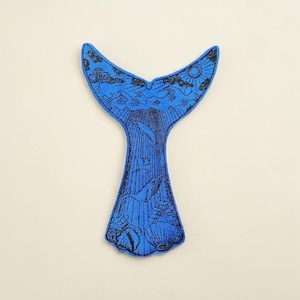 May include: A blue whale tail-shaped patch with a detailed ocean scene. The design includes waves, dolphins, a sun, and clouds, all in black against a vibrant blue background. The patch is likely for sewing or ironing onto fabric.