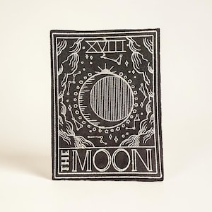 May include: Black and white embroidered patch featuring a tarot card design. The patch depicts a crescent moon, stars, and the words "THE MOON". The design is framed by decorative borders and the Roman numeral XVIII.