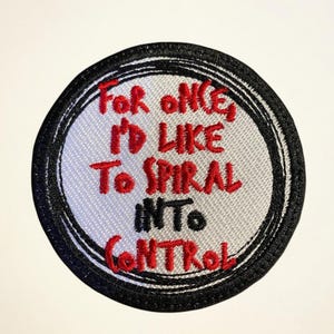 May include: Round embroidered patch with the text "For once, I'd like to spiral into control" in red, black, and white. The patch has a black border and a light gray background.