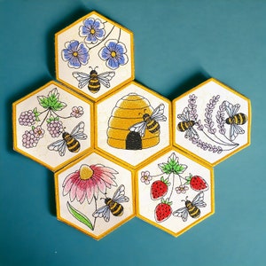 May include: Six hexagonal fabric patches with embroidered bee and flower designs. The patches are yellow, green, and red with black outlines. The patches are arranged in a honeycomb pattern.