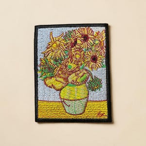 Puede incluir: Parche bordado con la pintura "Girasoles" de Van Gogh. El parche muestra un ramo de girasoles amarillos en un jarrón verde y amarillo, sobre un fondo azul claro con una base amarilla. El parche es rectangular.