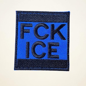 May include: Square patch with the text "FCK ICE" in black, embroidered on a blue background. The patch has a black border and is likely designed to be sewn or attached to clothing or accessories.