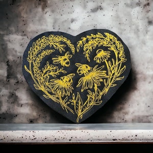 May include: A black heart-shaped patch with a gold embroidered design of bees and flowers.
