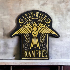 May include: Black and gold embroidered patch with a bird design and the text "Stay Wild Roam Free".