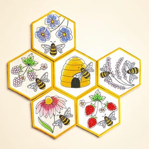 Puede incluir: Colección de parches hexagonales bordados dispuestos en forma de panal. Cada parche presenta un diseño diferente, incluyendo flores, bayas, una colmena y abejas. Los parches tienen un fondo blanco con ribete dorado.