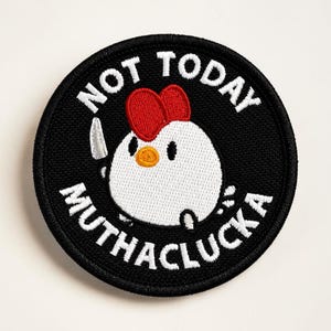Puede incluir: Parche bordado redondo negro con un dibujo de un pollo blanco sosteniendo un cuchillo. El pollo tiene una cresta roja y un pico naranja. El texto blanco en el parche dice: "NOT TODAY MUTHACLUCKA".
