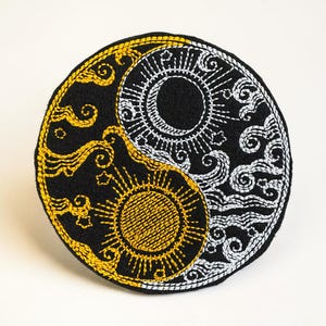 May include: Embroidered Yin and Yang symbol in black, gold, and white. The design features sun and moon imagery with intricate stitching. The circular patch is a decorative item, possibly for clothing or accessories.