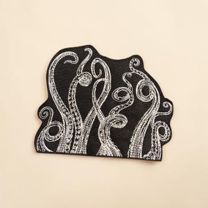以下が含まれることがあります： 黒い刺繍ワッペンで、白い糸で複数のタコの触手がデザインされています。触手は渦を巻いて伸びるような動きで描かれており、それぞれの触手の長さに沿って円形の吸盤のディテールがはっきりと確認できます。