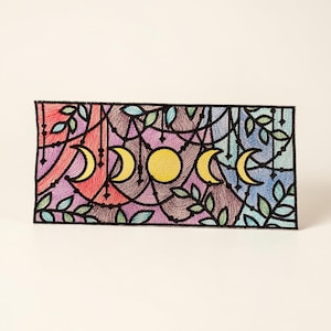May include: A rectangular patch featuring a colorful design of the phases of the moon. The artwork includes a yellow full moon and crescent moons in shades of yellow. The background has purple, red, and blue hues, with green leaves and black outlines.