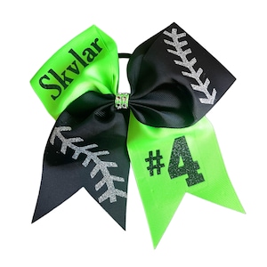 May include: A cheerleading bow with a lime green and black color scheme. The bow features the name "Skylar" in black text, silver glitter accents, and the number "4". The bow is tied with a rhinestone center.