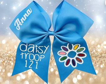 May include: A blue hair bow with a white daisy and the text "daisy troop 121" and "Anna" on it.
