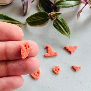 May include: A set of six orange Halloween-themed resin charms. The charms include a ghost, a witch's hat, a bat, a skull, and two bats.