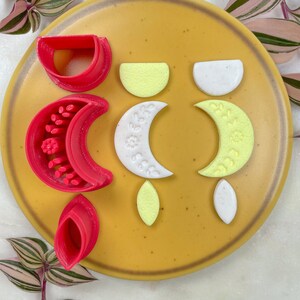 Może przedstawiać: Zestaw sześciu kolczyków z polimerowej gliny w trzech różnych kształtach: półksiężyc, półkole i łza. Kolczyki są w trzech kolorach: czerwonym, białym i żółtym. Kolczyki są ułożone na żółtym talerzu.