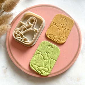 Może przedstawiać: Trzy foremki do ciasteczek na różowym talerzu. Foremki mają kształt siedzącej osoby. Foremki są wykonane z białego plastiku. Foremki znajdują się na różowym talerzu ze złotą obwódką.