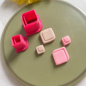 Może przedstawiać: Zestaw różowych, kwadratowych foremek do modeliny i kilka kwadratowych kawałków gliny w odcieniach różu i beżu. Foremki znajdują się na zielonym talerzu z żółtym kwiatem w tle.