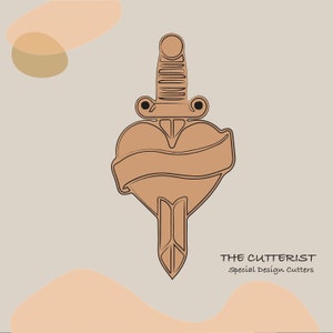 Könnte beinhalten: Ein braunes Herz mit einem Dolch, der durchstoßen wird, mit einem Banner um das Herz. Das Design ist für einen Ausstecher. Der Text unter dem Design lautet "THE CUTTERIST Special Design Cutters".