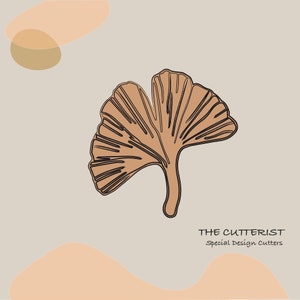 Puede incluir: Una hoja de ginkgo marrón con contorno negro, sobre un fondo gris claro con formas abstractas de color melocotón y marrón. El texto "THE CUTTERIST Special Design Cutters" está en la parte inferior de la imagen.