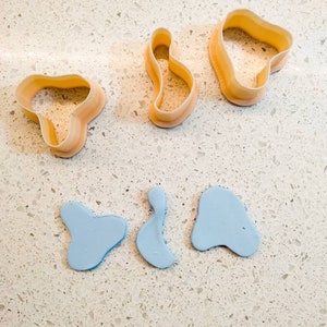 Könnte beinhalten: Drei Ausstecher aus Kunststoff in Form von abstrakten organischen Formen. Drei blaue Tonschichten sind ebenfalls abgebildet, die mit den Ausstechern ausgeschnitten zu sein scheinen.